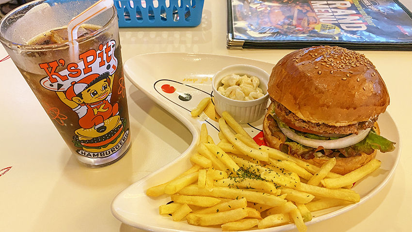 バーベキューバーガーセットの写真。ビーフパティと輪切された玉ねぎとトマト、レタスをふっくら厚みのあるバンズで挟んだ大きなハンバーガーと、付け合わせに揚げたてポテトとパスタサラダがある。