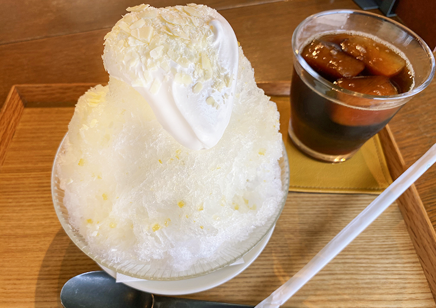 はちみつレモンクリームかき氷。大きなかき氷の上にはクリームとホワイトチョコがちりばめられている。氷の中にはレモンシロップの他にレモンピールが練り込まれているのが見える。 width=