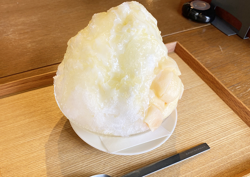 生桃のミルクかき氷。大きなかき氷に桃のシロップとミルクがかけられていて、氷の脇には桃の果肉がたっぷり添えられている。 width=
